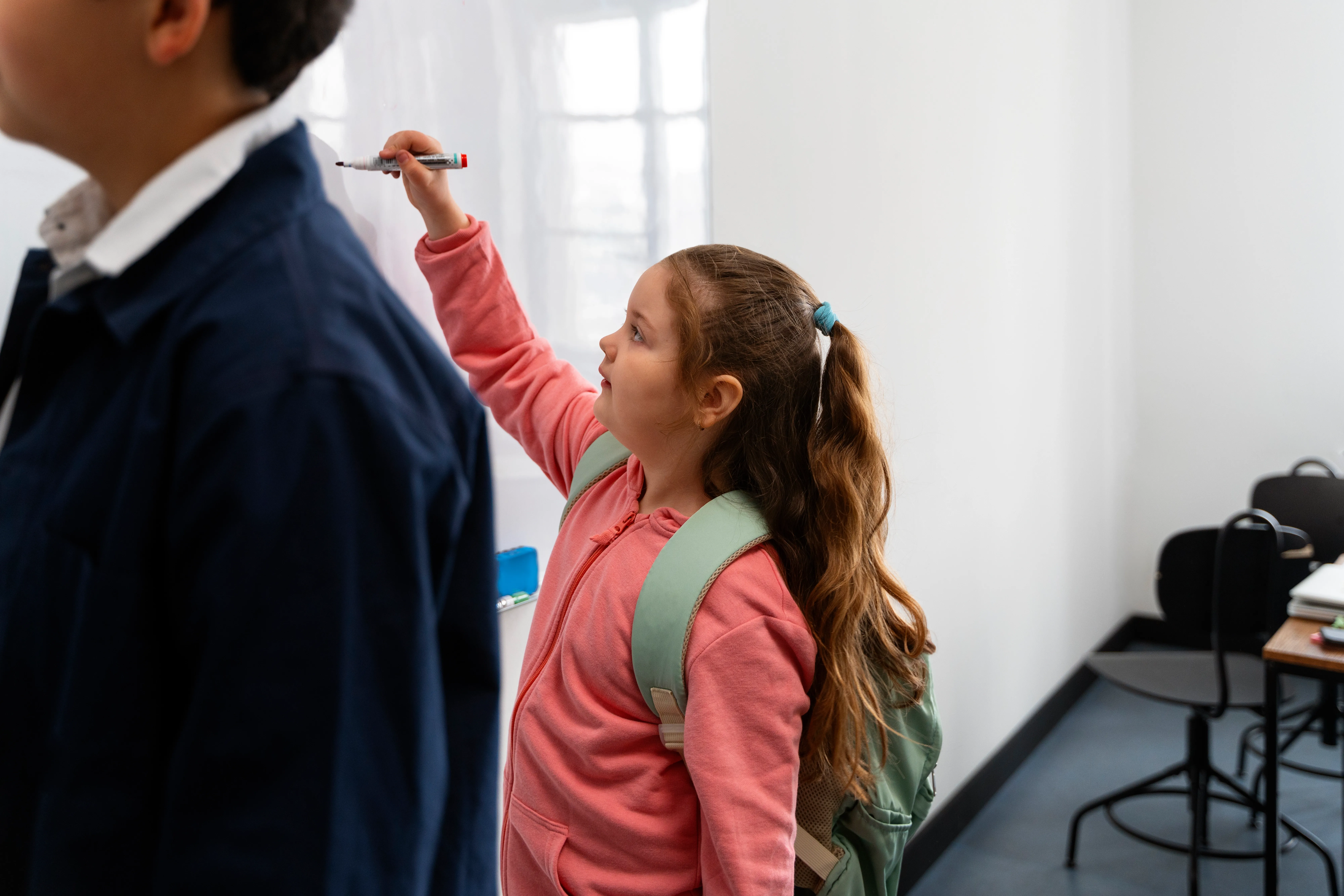 Criança escrevendo com canetão em quadro branco